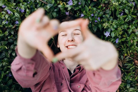Joyful young woman lying on a bed of blooming periwinkle flowers, smiling and playfully framing the
