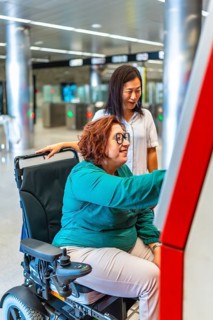 Vertical side view photo of a disabled woman and friend buying the ticket for the metro