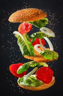 Ingredients of a burger with lettuce, tomatoes, onions and schnitzel floating freely on a dark