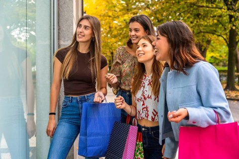Group of happy women friends walking together on a city street, looking at a shop window with