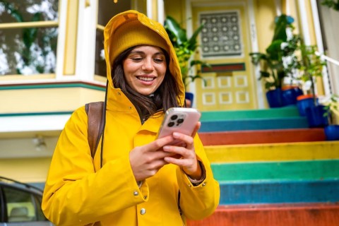 Woman in vibrant yellow raincoat and beanie smiling at smartphone on san francisco street, colorful