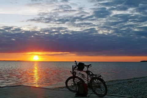 A bicycle is parked on the jetty as the sun sets over the sea in a colorful sky on the horizon