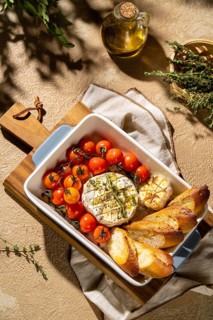 A delicious baked Camembert cheese served with cherry tomatoes and crispy bread in a vintage dish.
