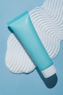 A sleek, blue cosmetic tube lies elegantly on a textured cream smear against a pastel blue