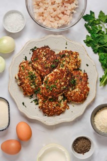 Fish patties are served on a plate. Chopped fish, herbs, onion, eggs, and seasonings are displayed