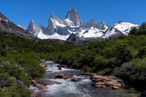 Mount Fitz Roy with snow-covered granite peaks, in the foreground a mountain stream between wooded