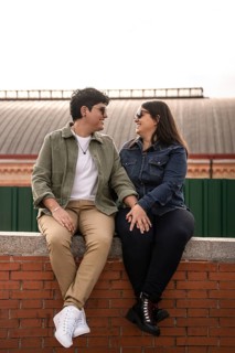A joyful lesbian couple sits on a brick wall, holding hands and sharing a tender moment. Both women