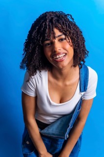 Portrait of a cheerful young woman with curly hair, wearing denim overalls and a white t shirt,