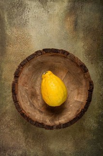 A single yellow fruit rests in a rustic wooden bowl, showcasing its vibrant color against a