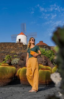 A woman in stylish, casual attire admires a traditional windmill in Lanzarote, set against a