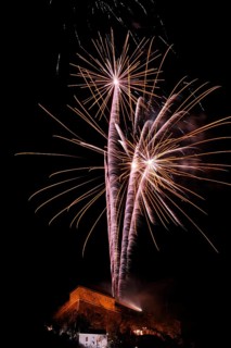 Golden firework tails sparkle majestically in the night over an illuminated building, New Year's