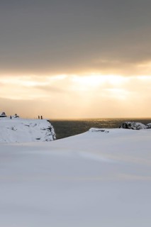 A serene Icelandic coastal landscape during winter, blanketed in snow, with a gentle sunset
