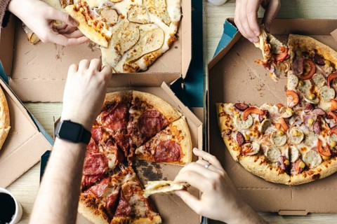 Top view of a group of unrecognizable friends gathers around the table, sharing slices of various