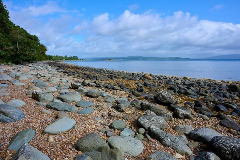 Rocky beach under clear blue sky with calm sea in the background, Tarbert, Loch Fyne, Kyles of