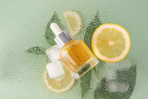 A cosmetic of citrus essence lies on a fresh, dewy surface with lemon slices and ice cubes. The