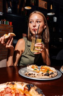 Woman sipping citrus lemonade while enjoying a slice of Margherita pizza topped with hard and