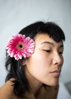 A serene portrait of an Asian woman with a pink flower tucked behind her ear. Her calm expression
