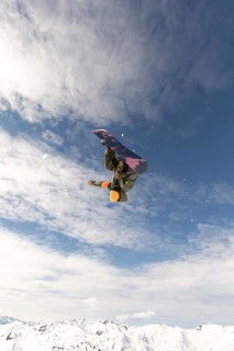 A daring snowboarder executes an impressive aerial trick against a backdrop of clear blue skies and