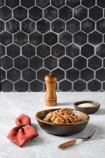 A bowl of spaghetti with pulled beef topped with fresh herbs and spices on a marble countertop,