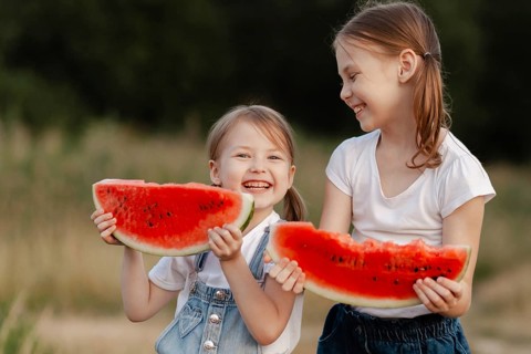 Two joyful children enjoy summer by sharing slices of fresh watermelon outdoors. Their laughter and
