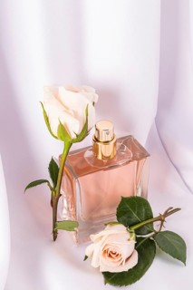 Elegant perfume bottle with golden accents surrounded by delicate white roses on a soft, draped