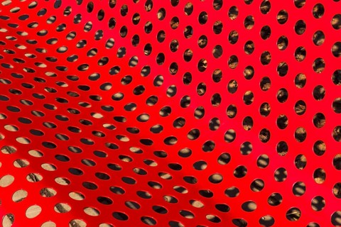 Close-up of vibrant red painted metal sitting bench and backrest with perforated round holes,