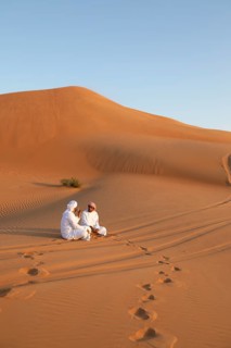 Bedouin men in white dishdashas sitting on a sand dune, Wahiba Sands desert or Rimal Al Wahiba or