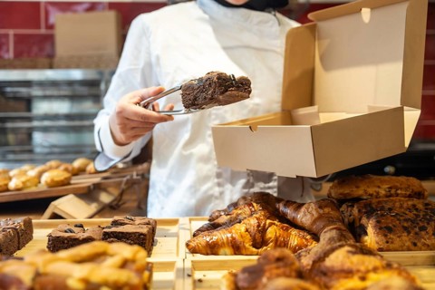 Baker wearing a chef uniform standing behind a counter, using tongs to carefully place a chocolate