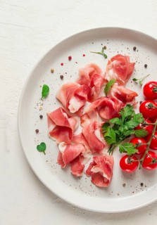 Sliced prosciutto, appetizer, with cherry tomatoes, on a white plate, top view