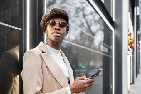 Chic black woman in an urban setting, wearing sunglasses and a hat, holding a smartphone The city