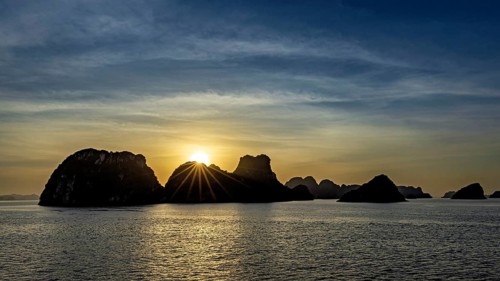 Boats sail past jagged rocks on a calm sea at sunset, sunset in Halong Bay in Vietnam