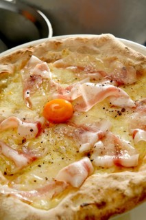 A freshly baked thin crust pizza topped with mozzarella, cured ham, and a vibrant egg yolk,
