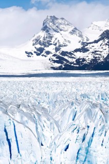 Perito Moreno glacier with rugged ice surface and blue crevasses, snow-capped Andean peaks in the