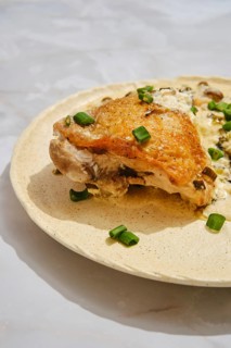 Close-up view of roasted chicken on a light-colored plate. Chopped green onions are scattered on