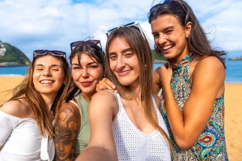 Four young women smiling for a beach selfie, enjoying sunny summer vacation together with sand, sea
