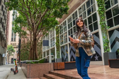 Woman standing on city street, smiling while navigating with a smartphone, representing urban