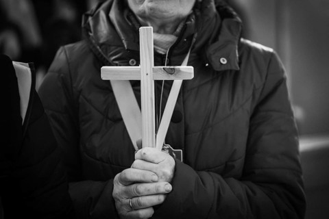 Black and white close-up of hands holding a simple wooden cross during a religious ceremony or