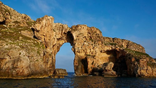 A massive rock arch stretches across coastal water, morning light, Tsichli Babas islet, Navarino