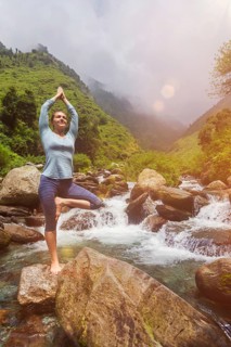 Woman in Hatha yoga balance yoga asana Vrikshasana tree pose at waterfall outdoors