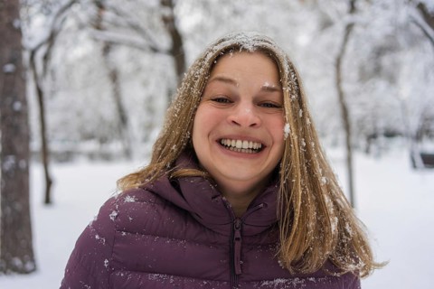 A cheerful woman in a warm jacket smiles joyfully, surrounded by a snowy winter landscape. Her hair
