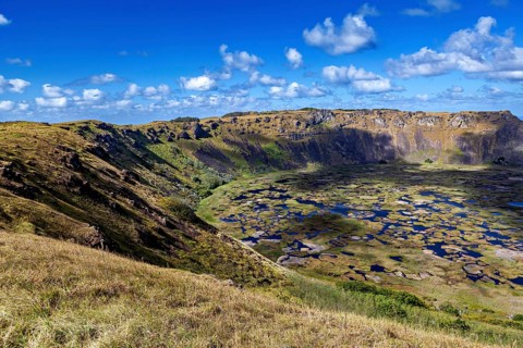 A far-reaching panorama of a crater lake surrounded by volcanic slopes under a clear sky, the Ranu