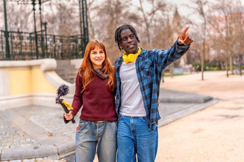 Two smiling content creators are working in a park, recording audio with a boom microphone and