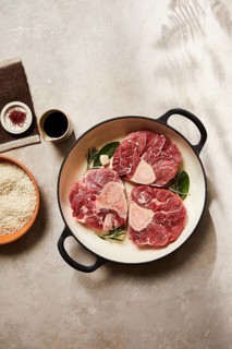 Fresh meat cuts displayed in a round pan, surrounded by natural ingredients like herbs and spices