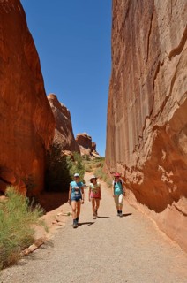 Three hikers walk through a narrow gorge between high sandstone walls, Arches National Park, Utah,