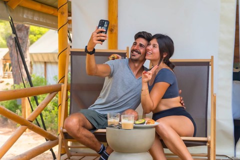 Young couple taking a selfie with smartphone while having breakfast outside their luxury tent