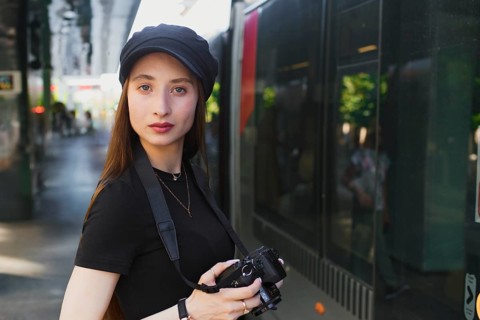 Young female photographer in urban setting, wearing casual attire, holding a camera. She stands