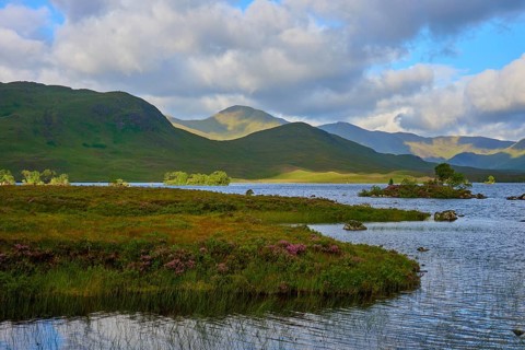 A lake with mountains in the background under a partly cloudy sky surrounded by green nature,