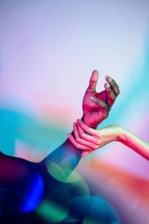 A close-up of multiethnic hands touching, illuminated by vibrant multicolored lighting. This image