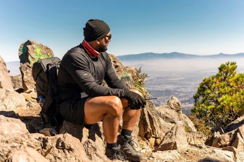A man in hiking gear sits on a rocky mountain summit, overlooking a vast, misty landscape The scene
