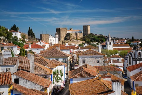 View the charming town of Obidos in Portugal, featuring a medieval castle and vibrant rooftops